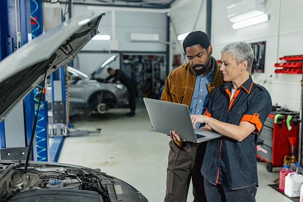 A customer shares insights with a mechanic while analyzing car engine details using a laptop in a well-equipped automotive workshop setting.