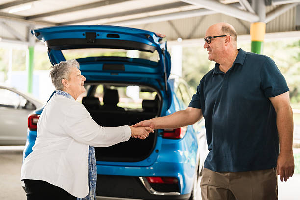 Car owner shaking hands with a used car buyer beside a blue vehicle after agreeing on a sale